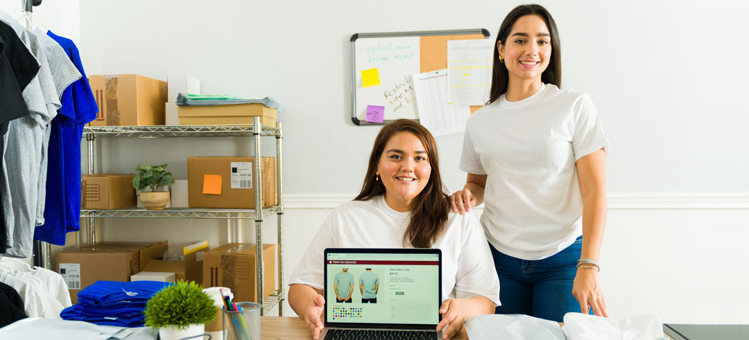 Mujeres jóvenes empresarias mostrando una tienda de camisetas en su ordenador